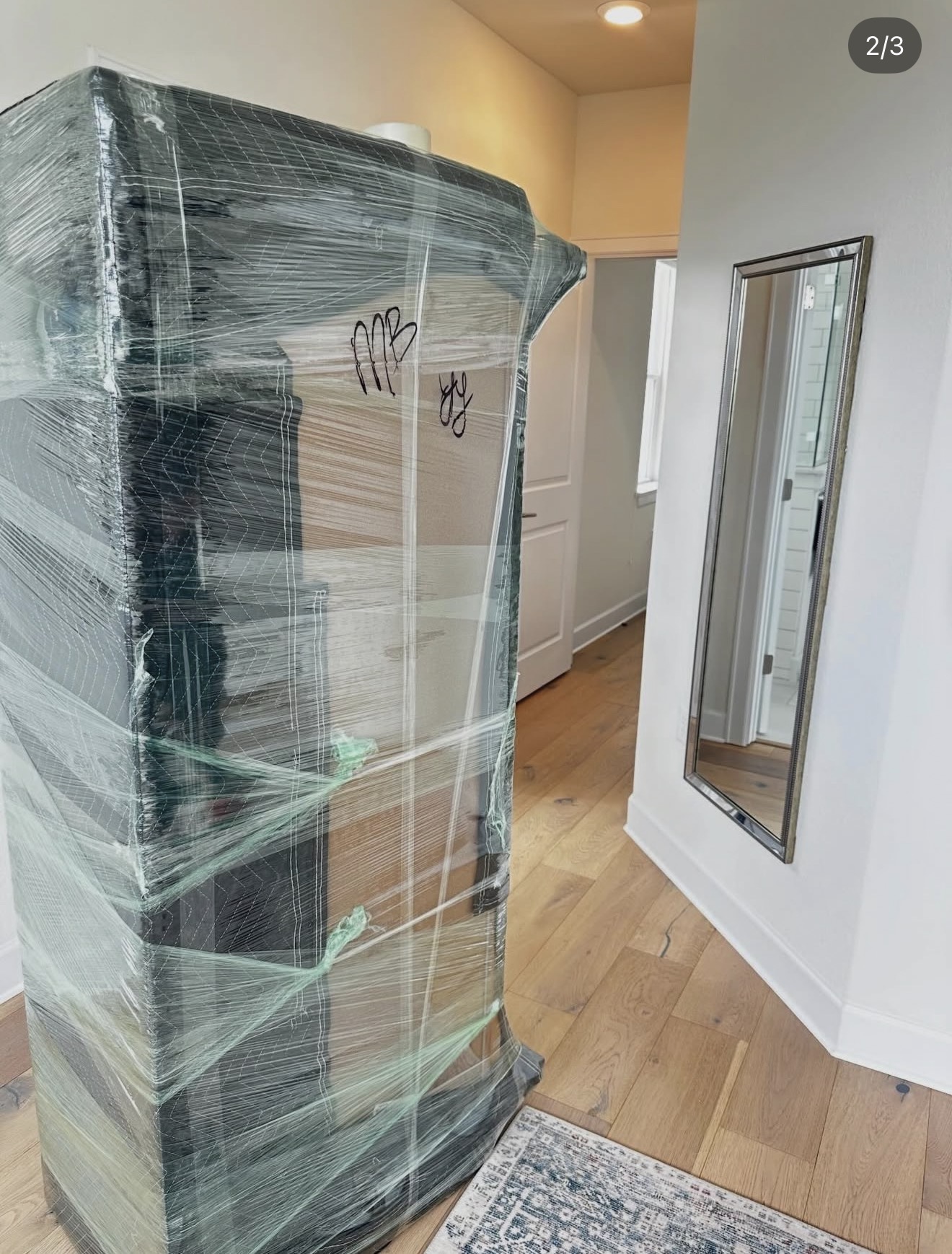 Tall wooden cabinet fully shrink-wrapped in stretch film and labeled, ready to be moved without damage