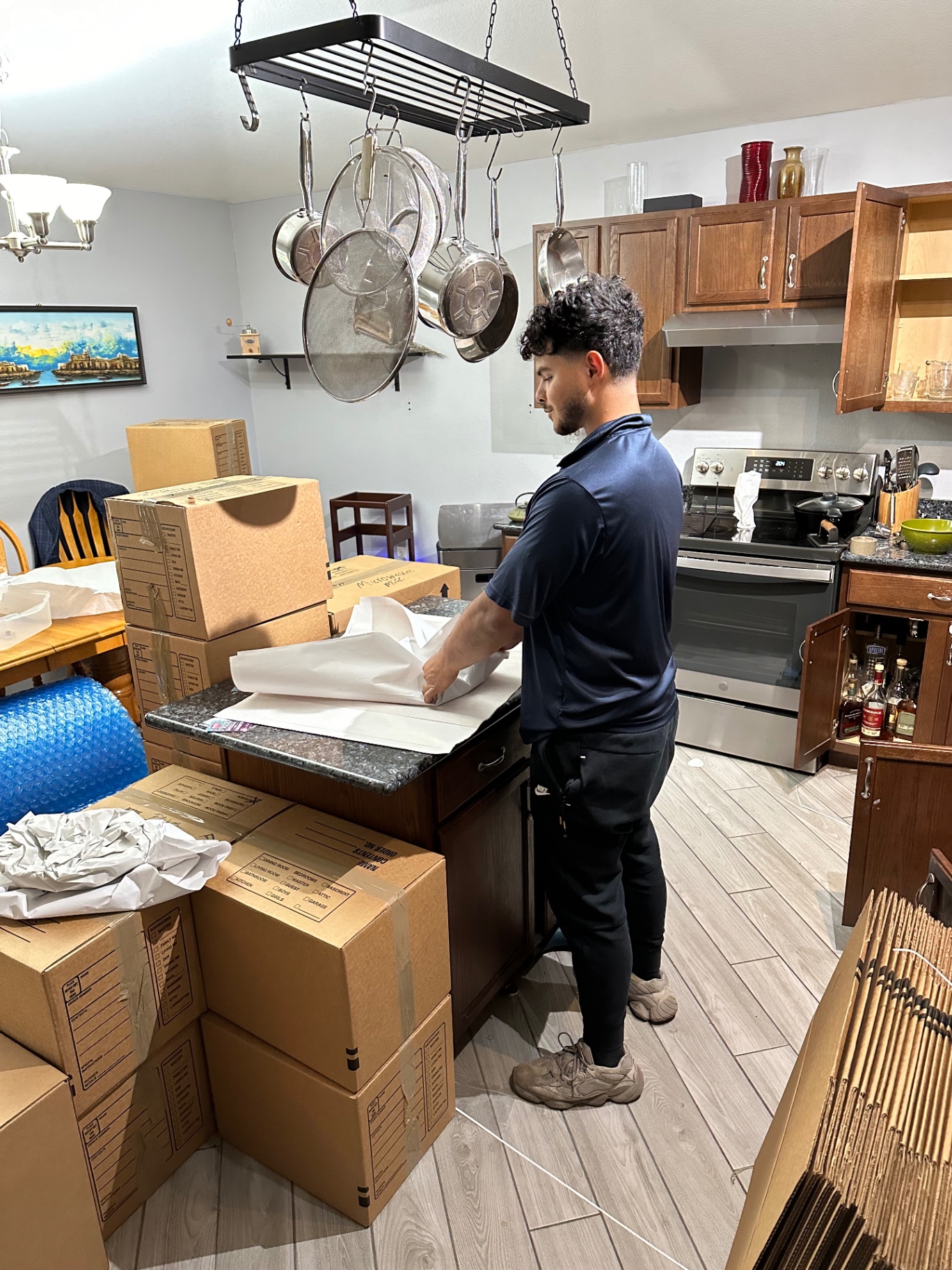 Mover in a navy polo carefully wrapping kitchenware in packing paper next to labeled moving boxes
