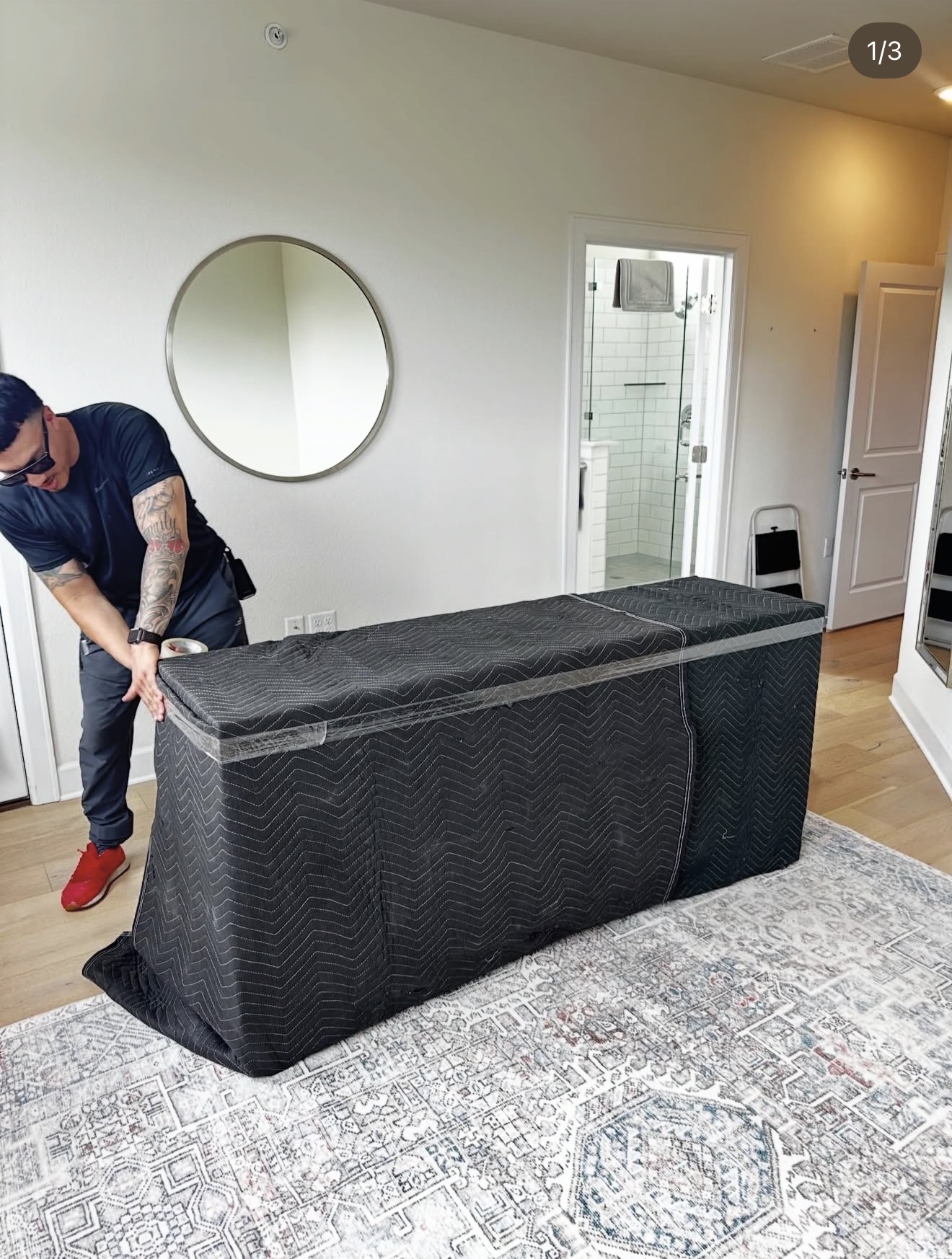 Lovable Moving crew member securing a moving blanket around a long console with stretch wrap in a bedroom