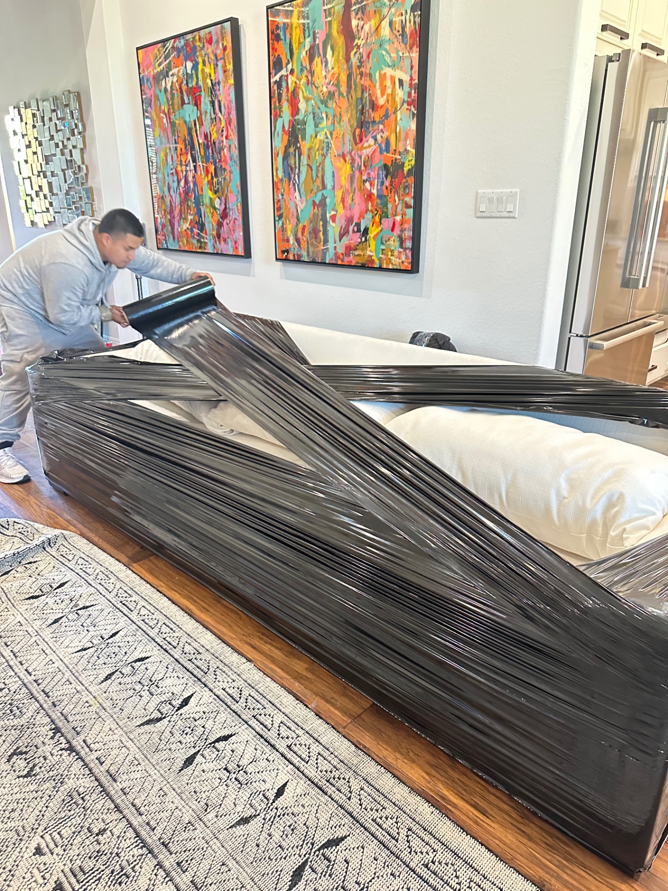 Mover shrink-wrapping a white sofa in black stretch film to protect it during transit