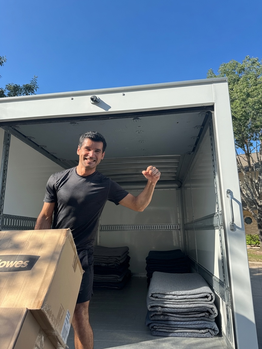 Smiling Lovable Moving crew member flexing while carrying a box out of a loaded moving truck in Austin, Texas