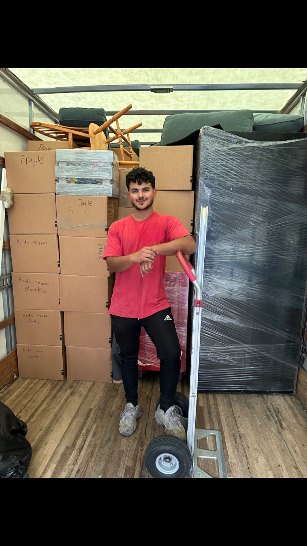 Lovable Moving crew member standing beside a fully loaded truck packed with labeled boxes and a wrapped mattress