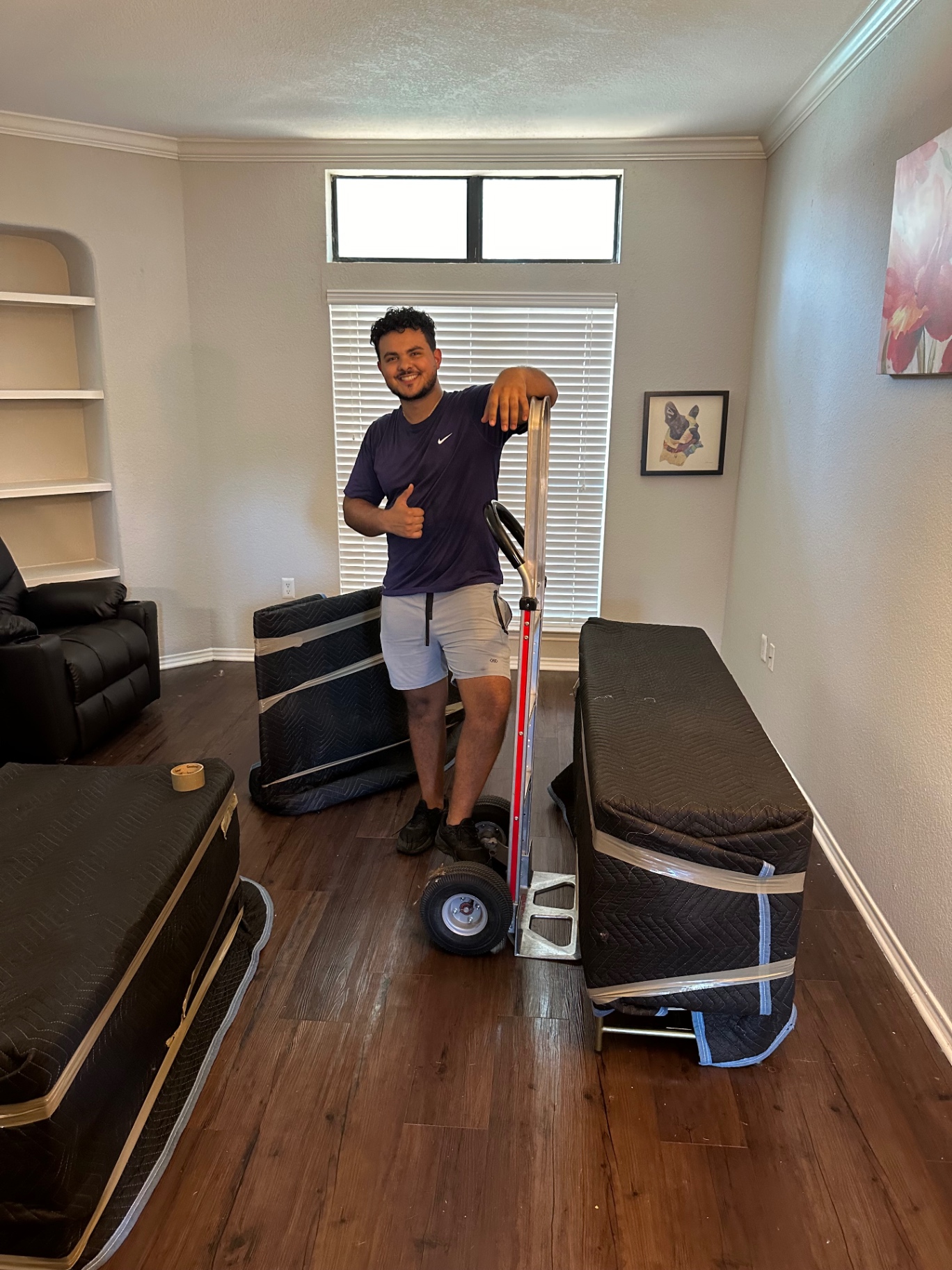 Lovable Moving crew member with a hand truck beside mattresses padded and wrapped for a move